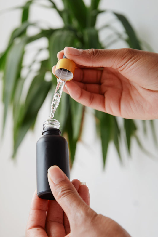 Hands holding a black dropper bottle of face oil