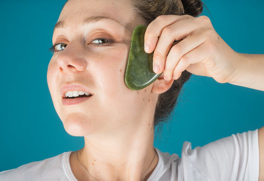 A woman using a jade face massager along her cheekbone