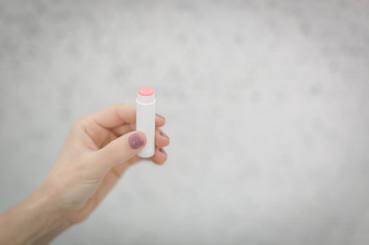 A slim lip balm tube standing on a pale surface