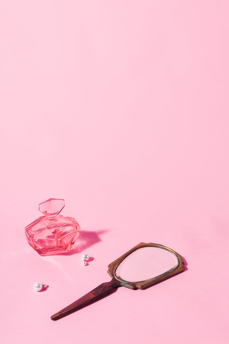 A perfume bottle and earrings in front of an antique mirror