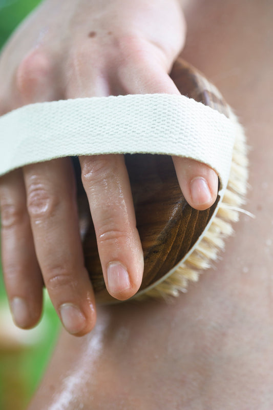 A wooden scrub brush being used on skin