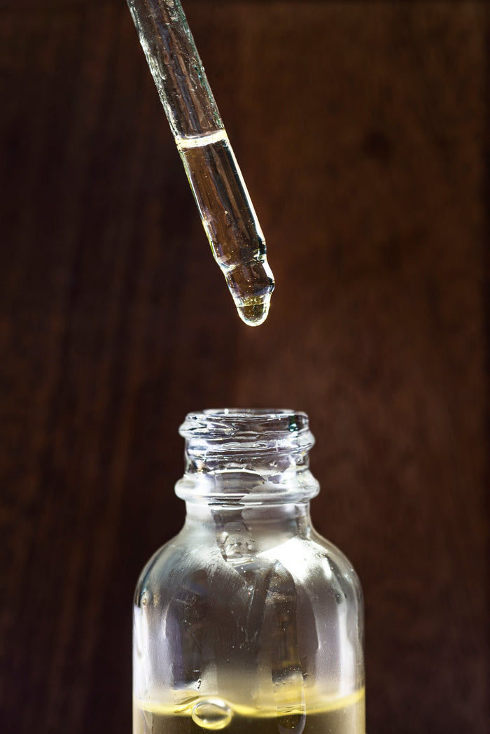 A glass jar of face oil with a dropper held above it