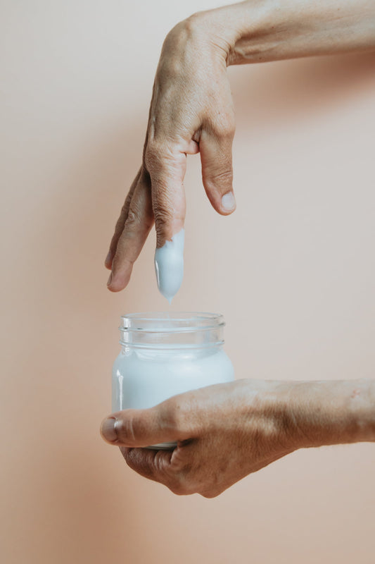 A hand beside an open glass jar of hand cream