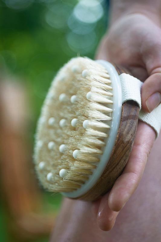 A hand holding a wooden dry-brush body exfoliator
