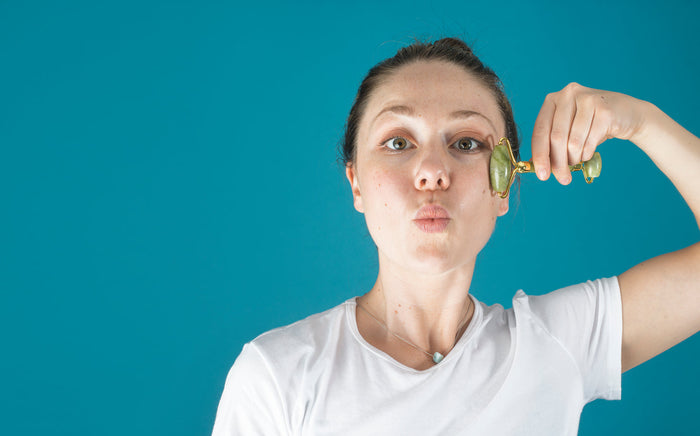 A woman using a jade face roller along her cheekbone